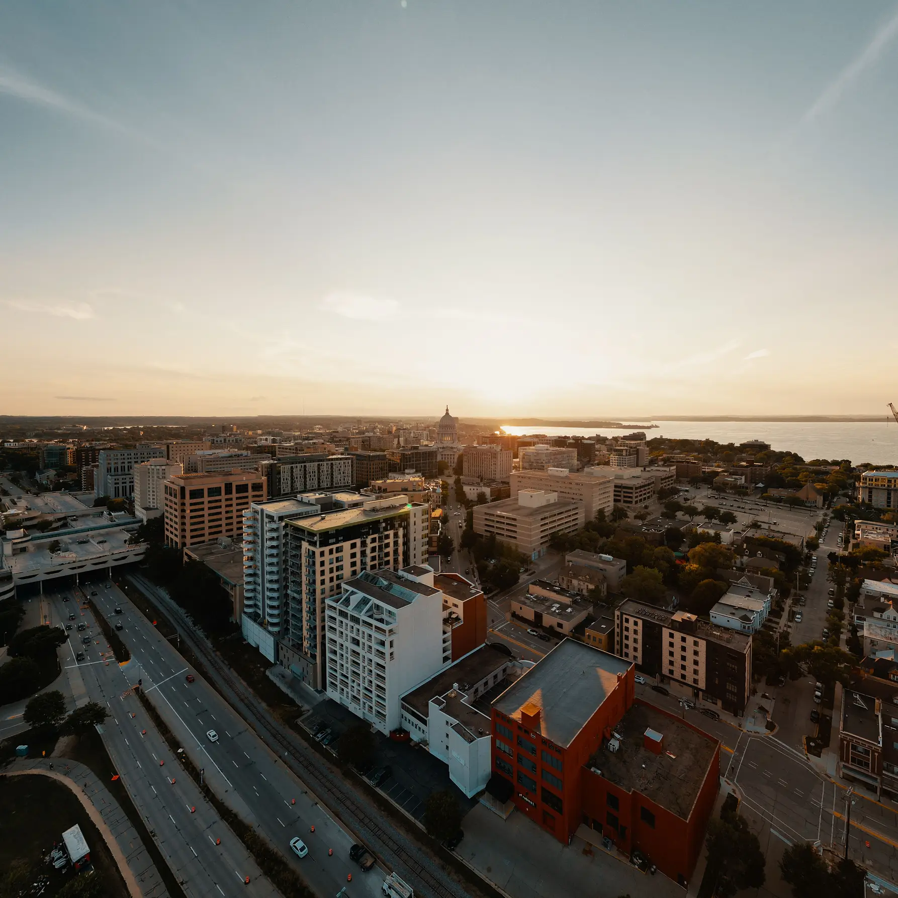 Aerial view of a city with tall buildings and roads at sunrise, sunlight illuminating the skyline—like watching your credit union savings account grow with each new day.