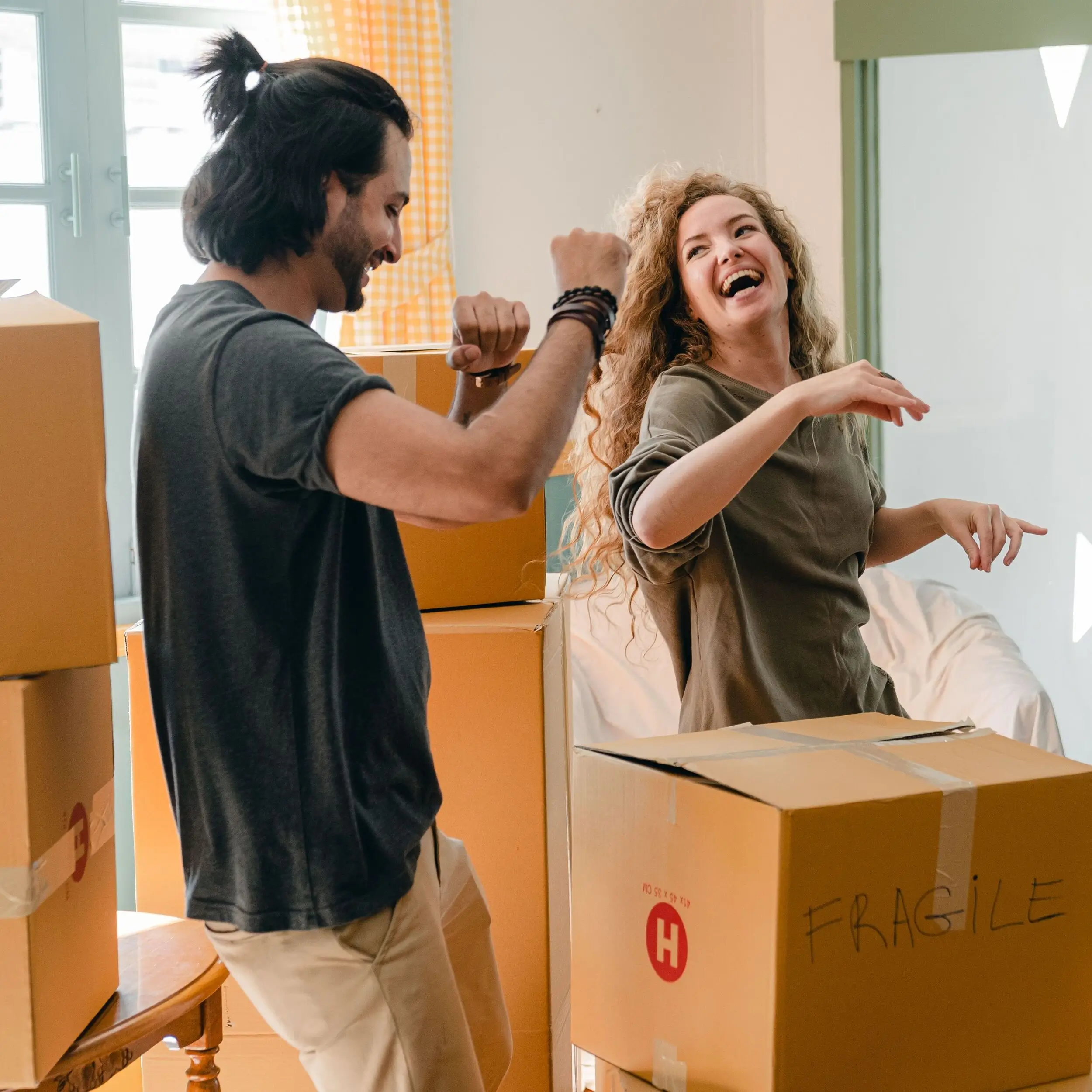 Two people laughing and dancing among moving boxes in a bright room, celebrating their new home together after securing it with an FHA loan.
