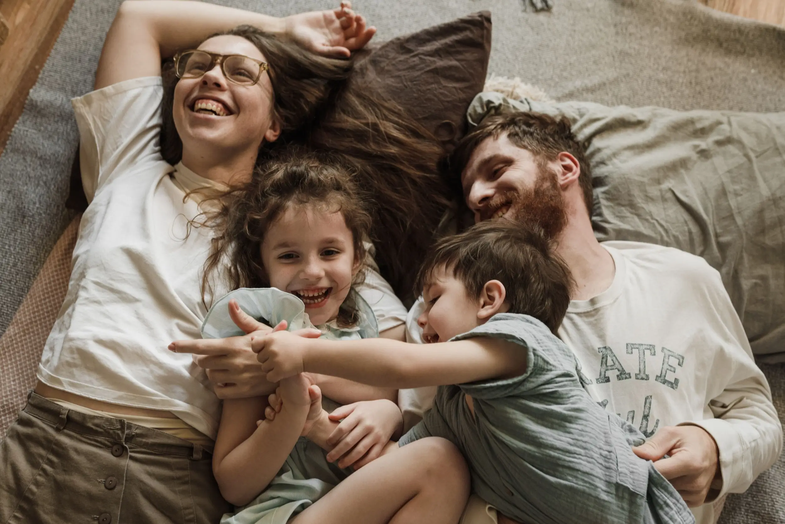 A happy family of four lies on a blanket, smiling and laughing together, enjoying a cozy moment while discussing their plans to check the latest auto loan rates.