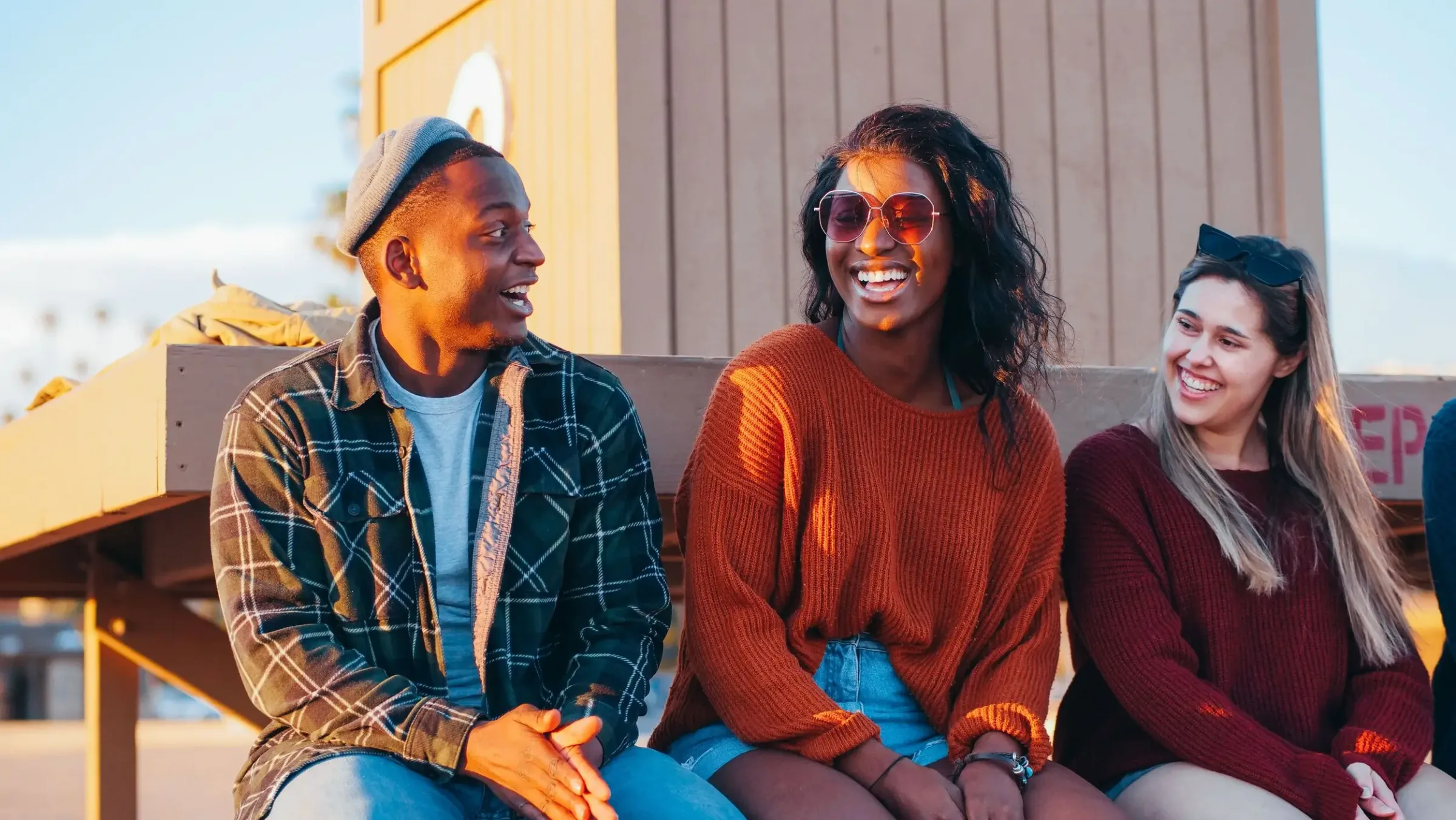 Three friends in casual clothes laugh and enjoy a sunny day together outside the local Linden Credit Union.