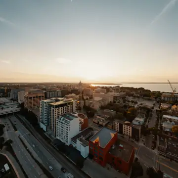 Aerial view of a cityscape at sunset, featuring tall buildings, roads, and a community credit union near the body of water under a clear sky.