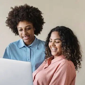 Two people smiling and looking at a laptop together against a plain background, exploring services from their local community credit union.
