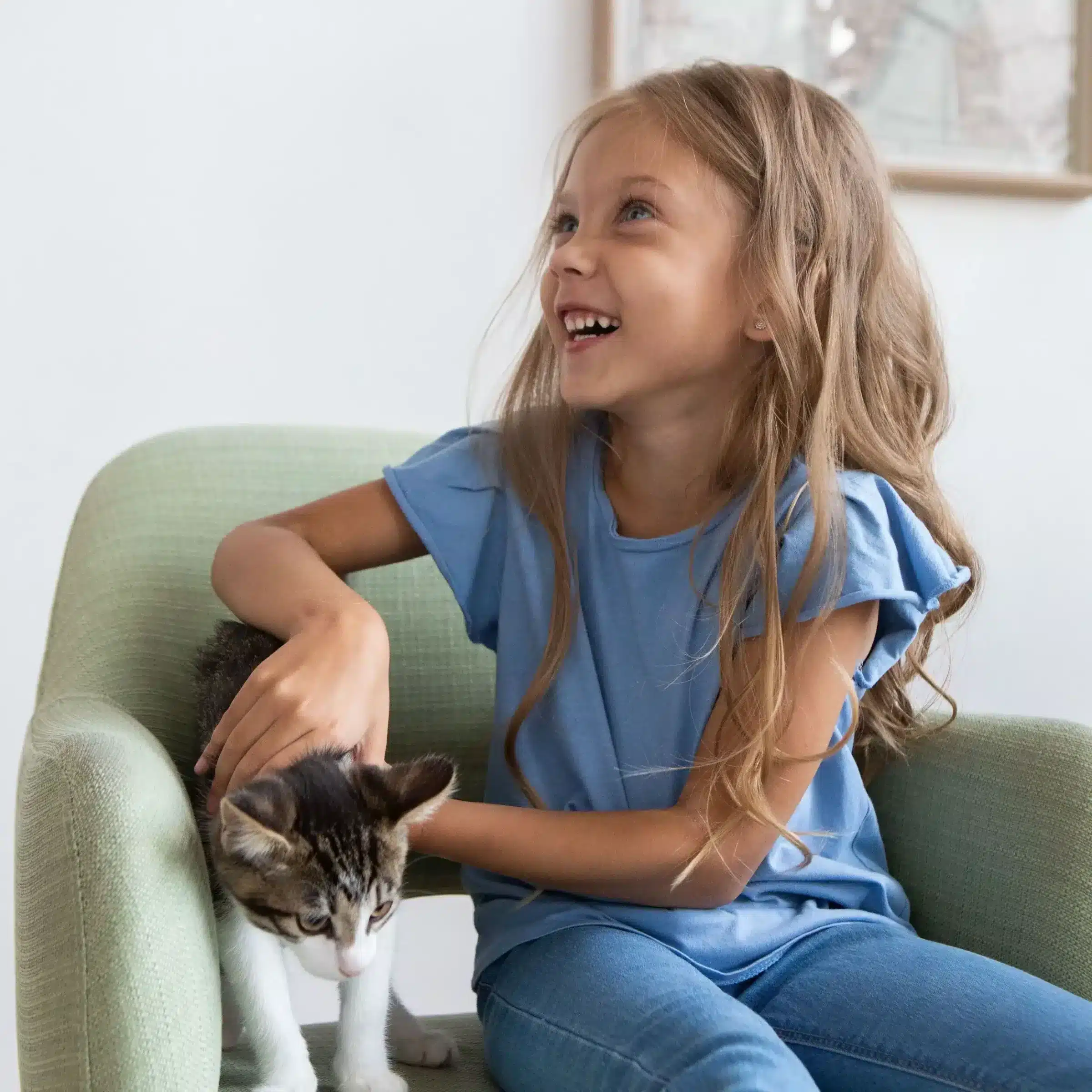 Smiling young girl in a blue shirt sits in a green chair, gently petting her cat while dreaming about her new youth savings account.